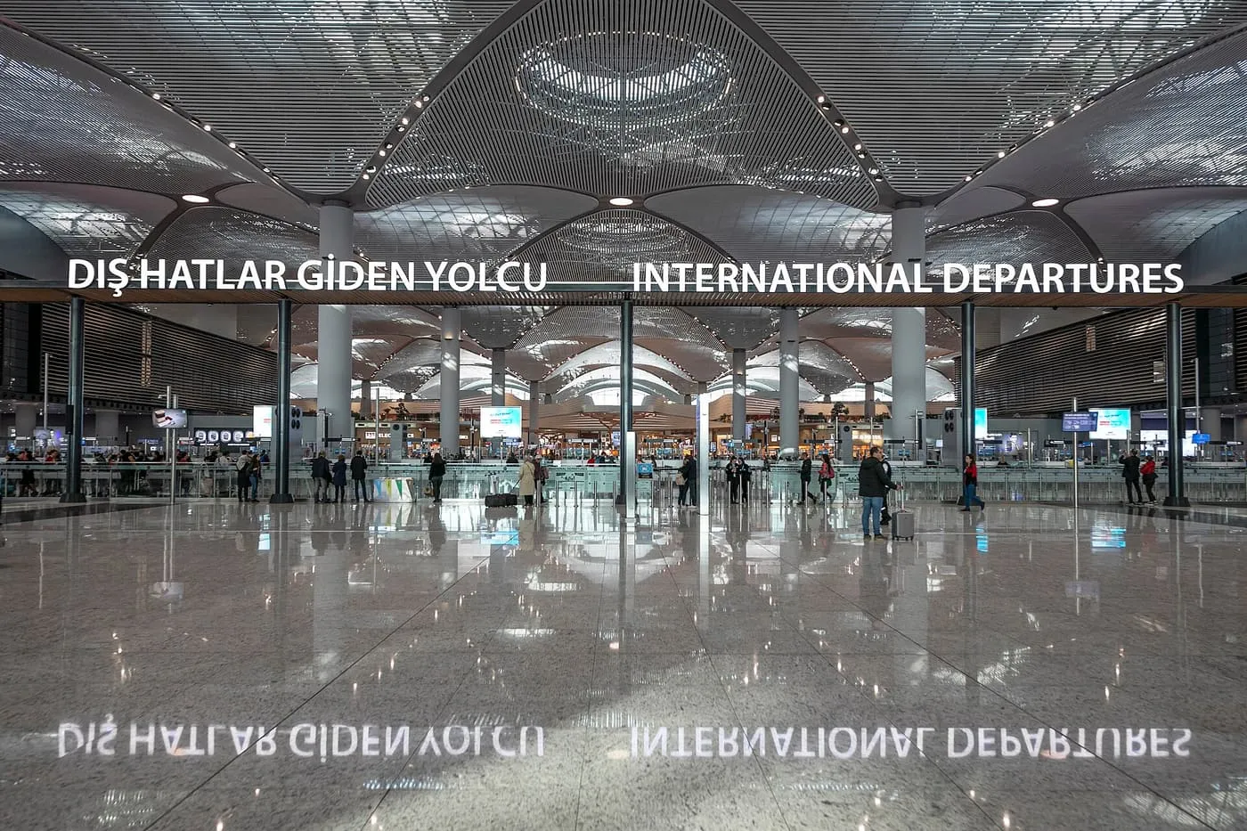The international departures hall at Istanbul Airport, with a sweeping ribbed ceiling, a bilingual sign over the check-in area and a polished floor reflecting the lettering