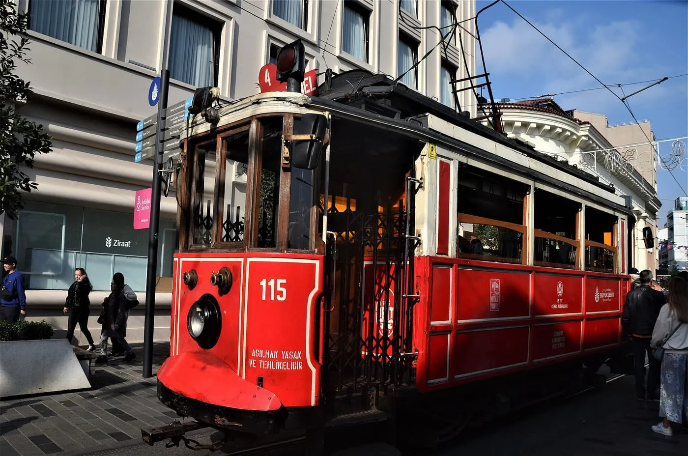 A red nostalgic tram on İstiklal Caddesi with pedestrians on the pavement
