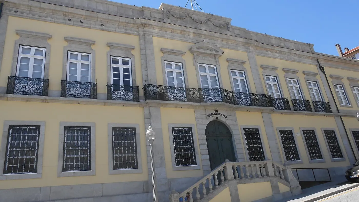 The pale yellow front of the Instituto do Vinho do Porto building, number 27, with iron balconies and a stone staircase to the door