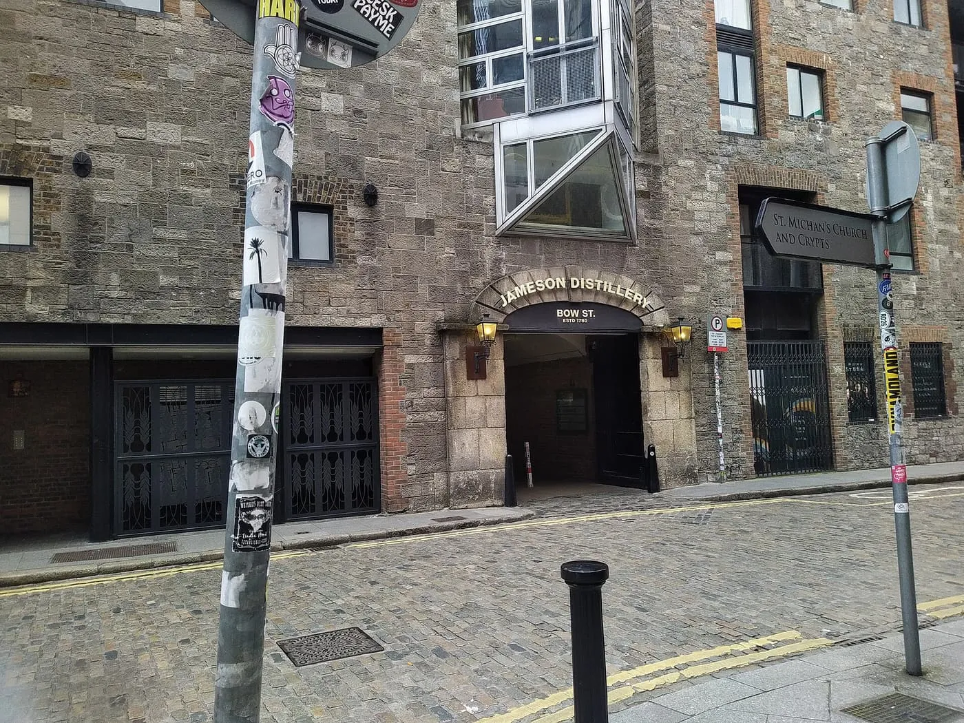 The stone front of the Jameson Distillery on Bow Street, with the Jameson Distillery Bow St. sign over an arched doorway on a cobbled street