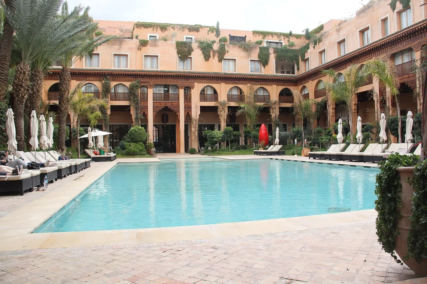The courtyard pool at Les Jardins de la Koutoubia, with sun loungers along one side and the hotel's arcaded galleries behind