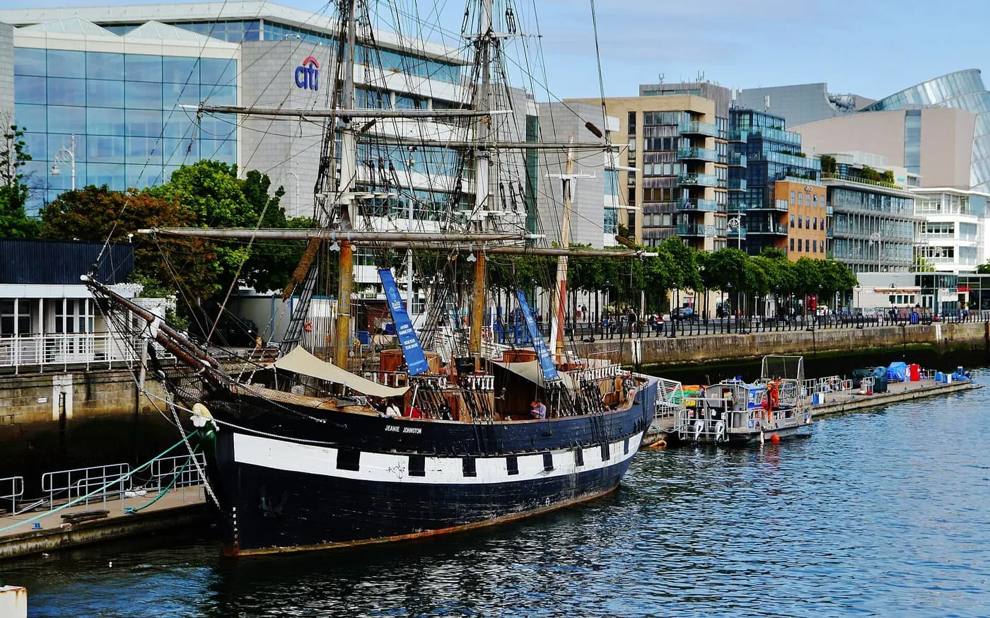 The black-hulled three-masted Jeanie Johnston moored on the Liffey with modern Docklands offices behind