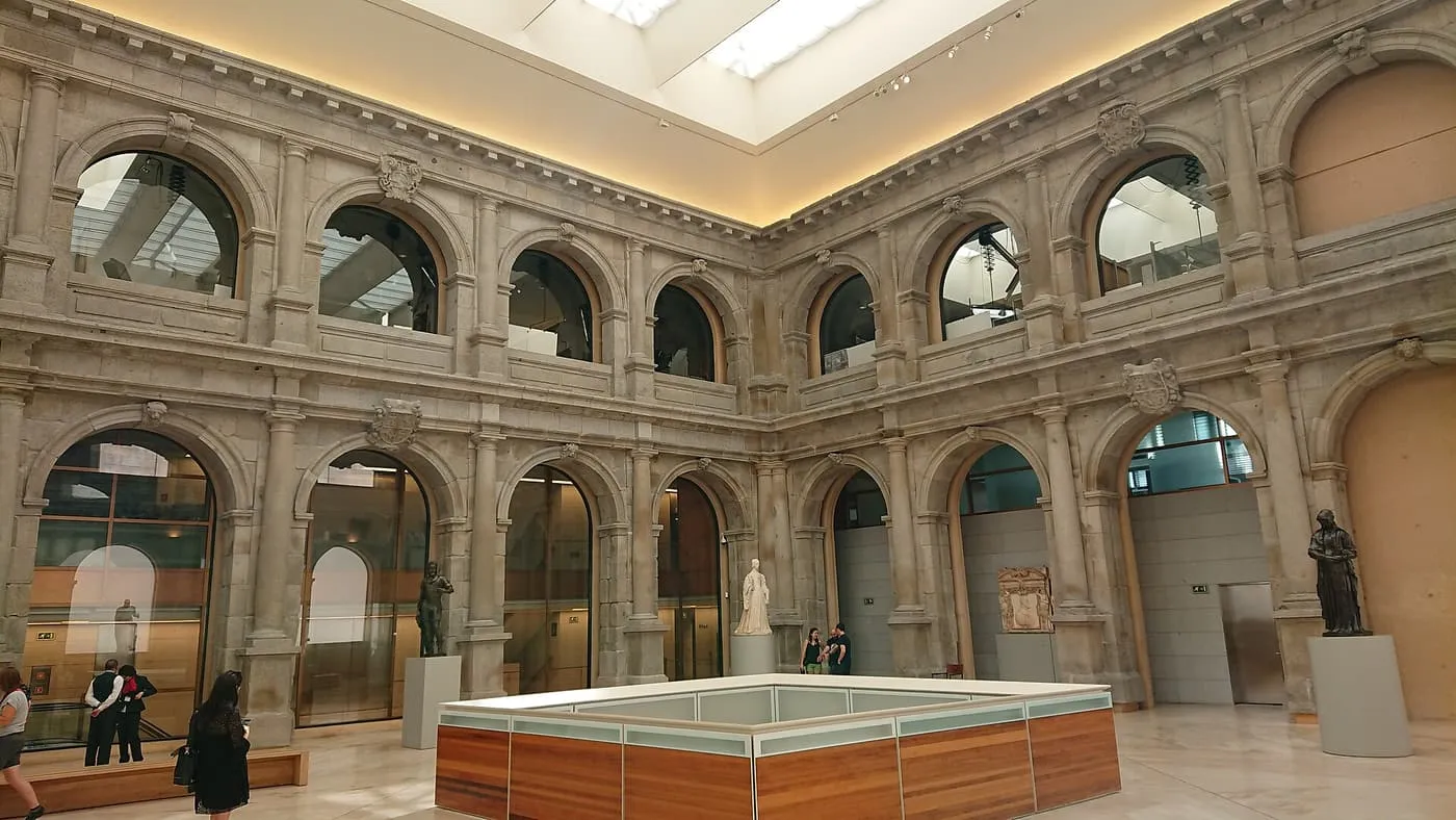 The restored stone cloister of the Jerónimos inside the Prado extension, with arched glass openings and a skylight overhead