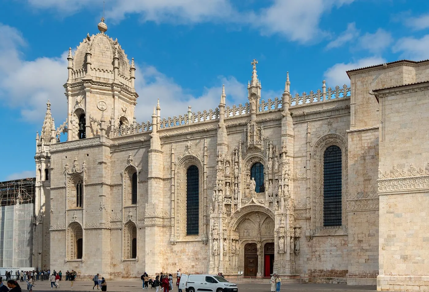 The south front of the Jerónimos Monastery church, with its carved portal, buttresses and bell tower, seen across a street