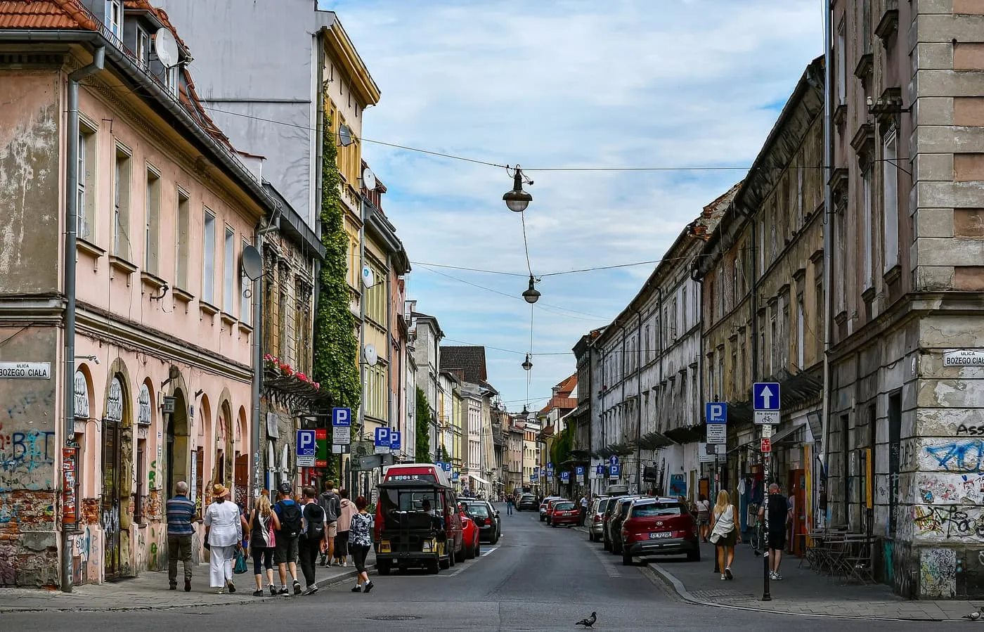 Józefa Street in Kazimierz, lined with faded townhouses, with walkers on the pavement and a small tourist vehicle parked at the kerb