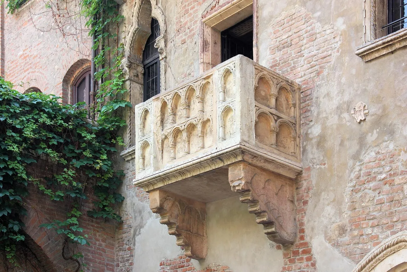 The stone balcony on the courtyard wall of Juliet's House in Verona, with ivy climbing the brick wall beside it