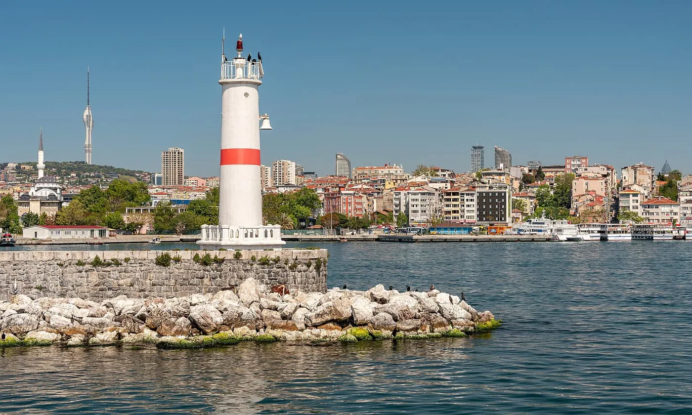 A white lighthouse with a red band on a breakwater off Kadıköy, with the Asian-side skyline behind