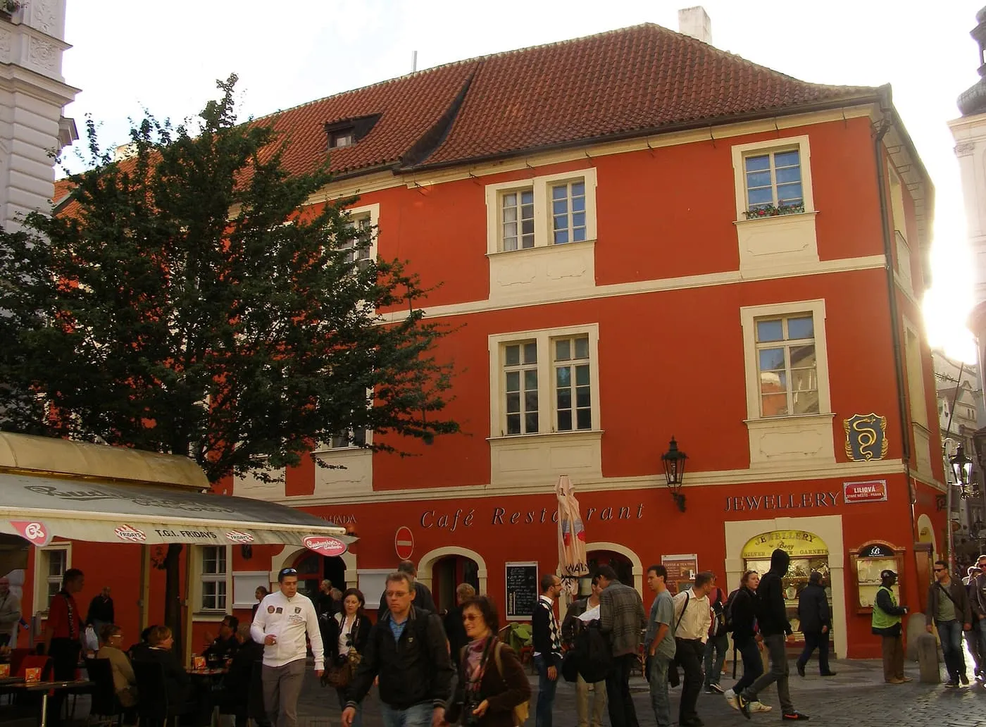 The House at the Golden Snake, a three-storey red house with café tables outside, on the corner of Karlova and Liliová streets