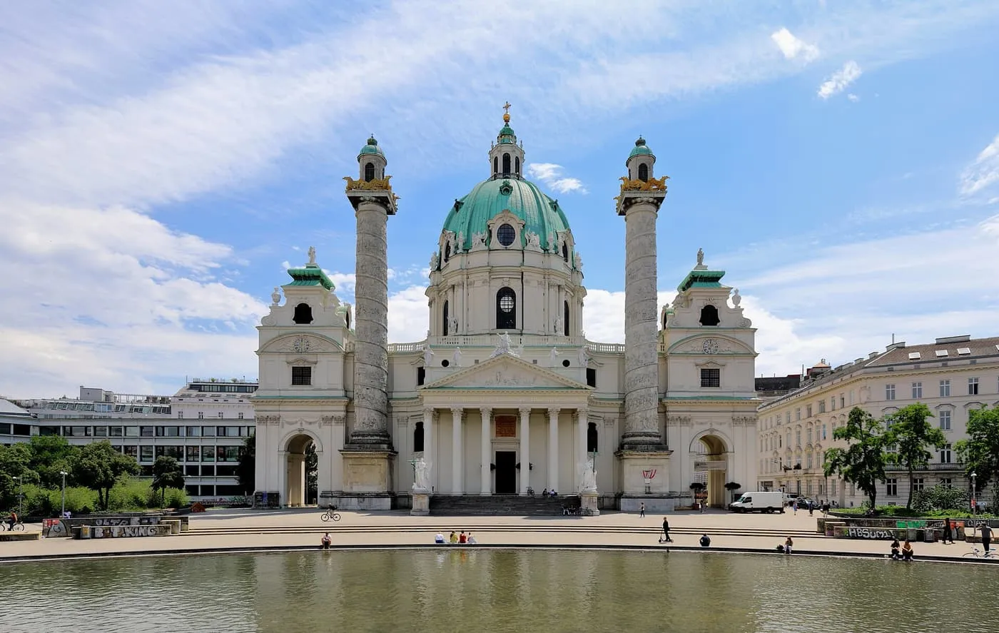 The Karlskirche with its green copper dome and two relief-wrapped columns, across a wide pool under a blue sky