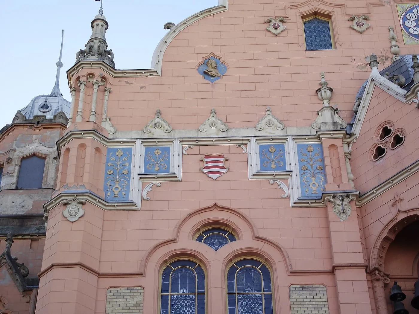 The pink front of Kecskemét Town Hall, decorated with blue tile panels and a striped coat of arms