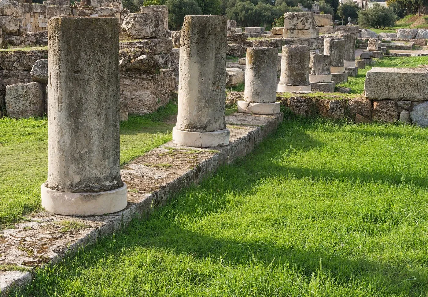 A row of column drums on white marble bases in the grass among the ruins of the Kerameikos