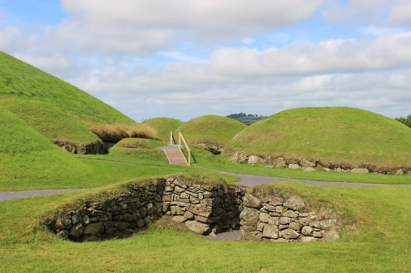 Grass-covered passage tomb mounds at Knowth with a dry-stone-lined opening in the foreground and a path between them