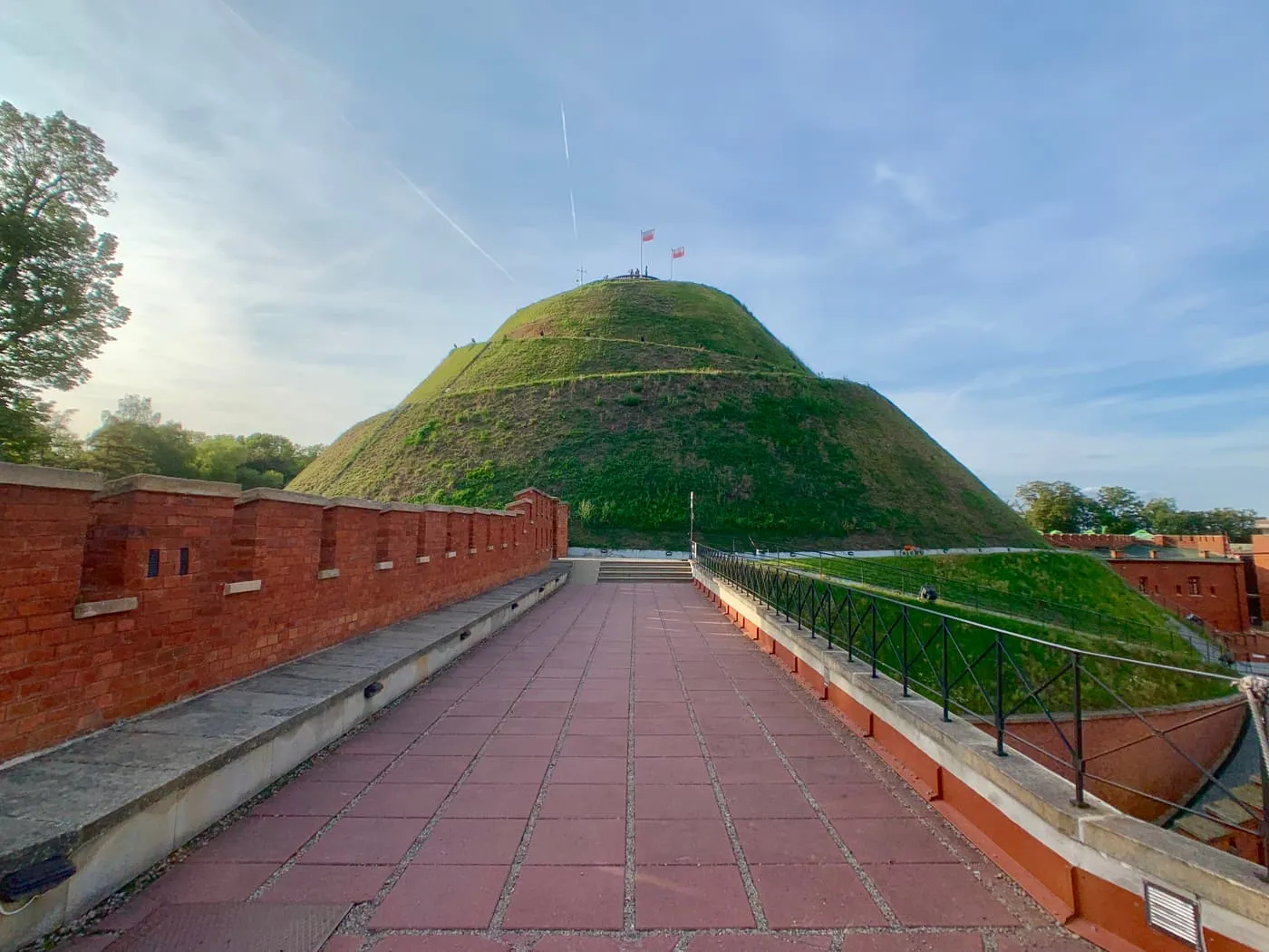 The Kościuszko Mound, a grassy cone with a paved path leading toward it along a red-brick wall