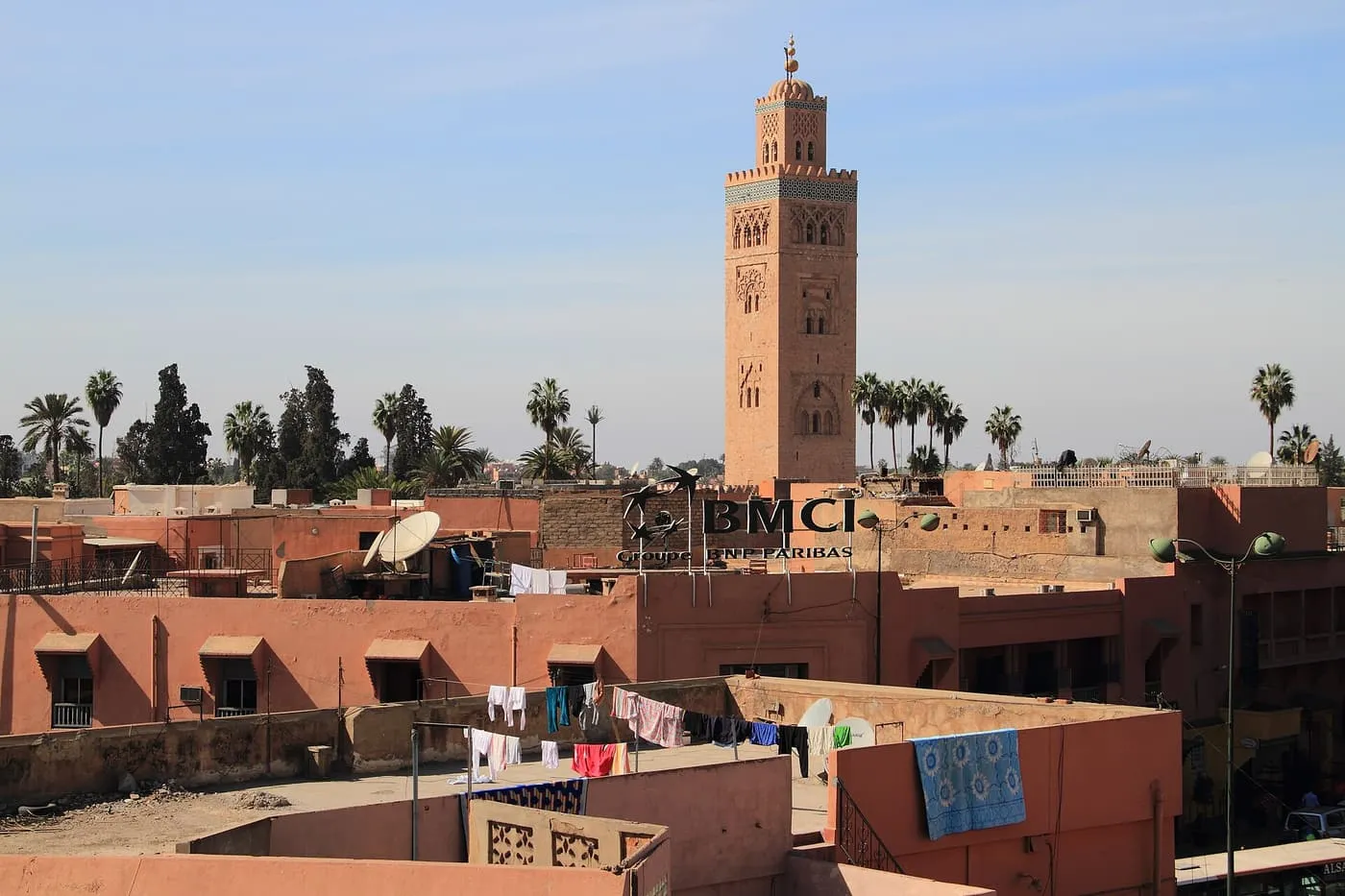 The Koutoubia minaret rising above the flat pink roofs of the medina, with washing hung out on a terrace and palm trees behind