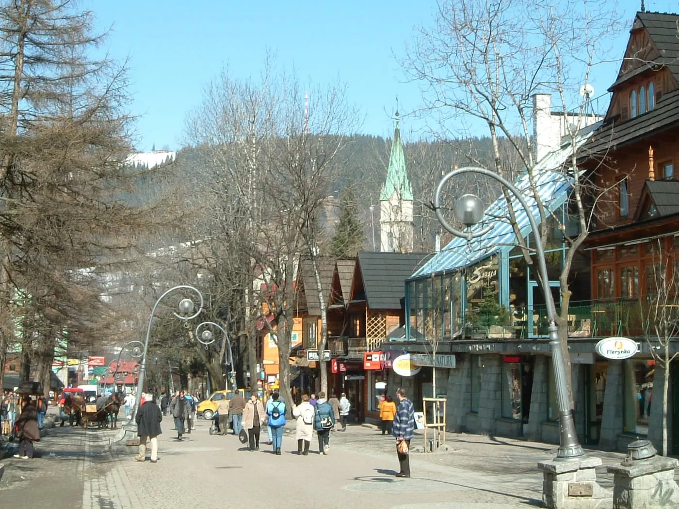 Walkers on Krupówki, the pedestrian street in the centre of Zakopane, with timber buildings and a church spire