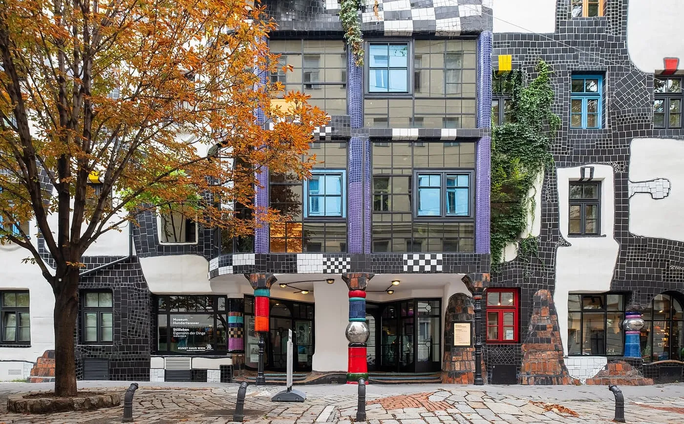 The KunstHausWien, a façade of black and white checked tiles with purple columns, coloured pillars at the entrance and an autumn tree at left
