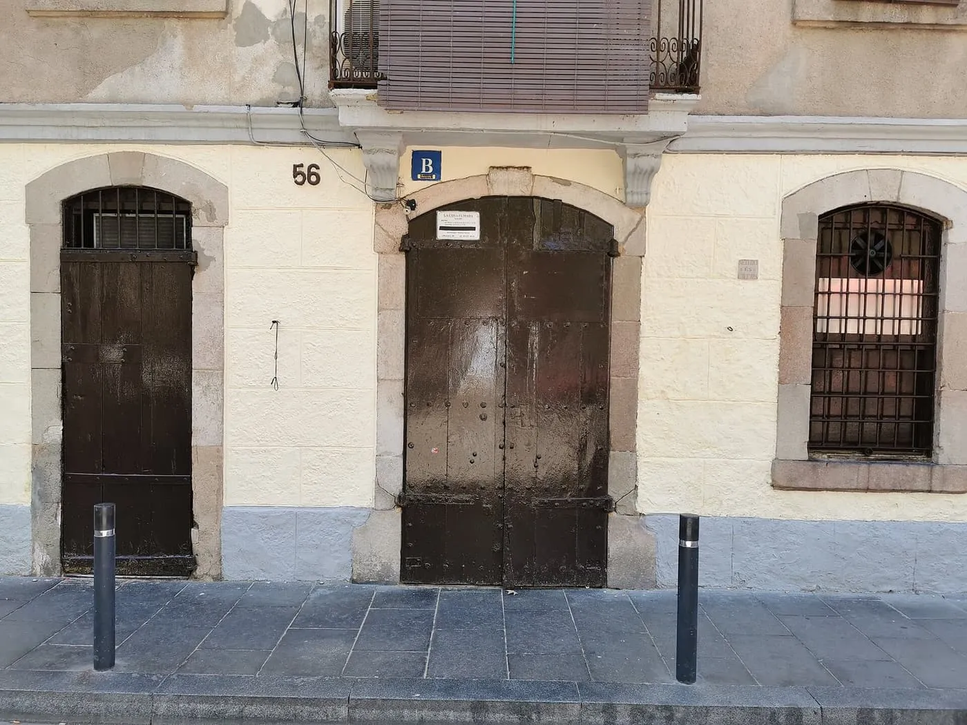 The dark double door of La Cova Fumada under the number 56 on Carrer del Baluard, between two barred windows