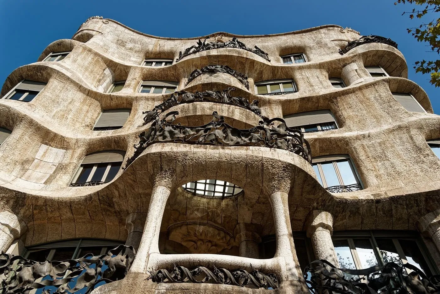 The rippling stone façade of La Pedrera seen from the pavement, with wrought-iron balconies and a wide entrance arch below