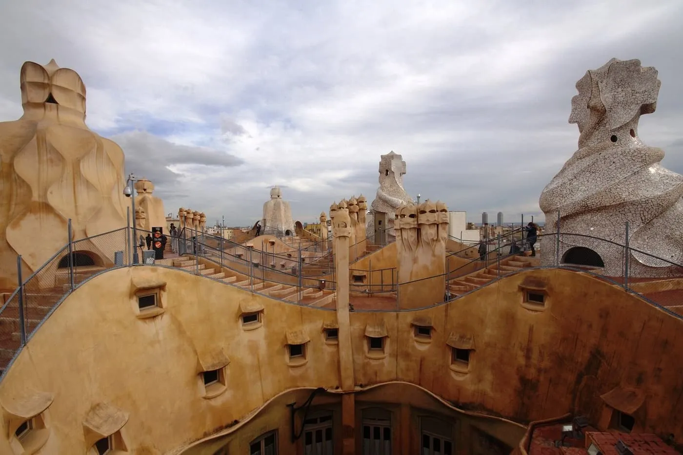 The rooftop of La Pedrera: staircase towers and sculpted chimneys, some clad in white mosaic, above the curving wall of a courtyard