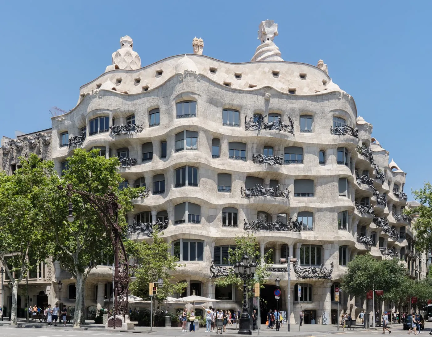 The rippling stone front of La Pedrera on its corner, with wrought-iron balconies, trees below and a clear blue sky