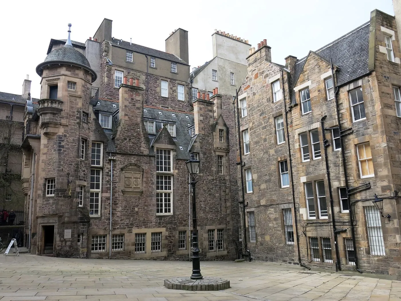 A stone courtyard with a lamp post in the middle, ringed by tall old stone houses with a round corner turret