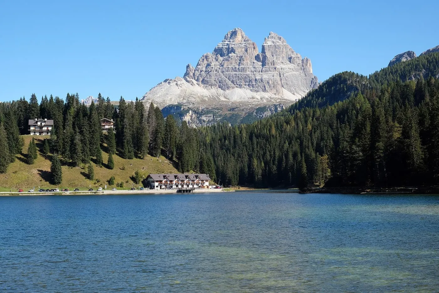 Lake Misurina with a forested shore and a lakeside building, and the Tre Cime di Lavaredo rising above the trees