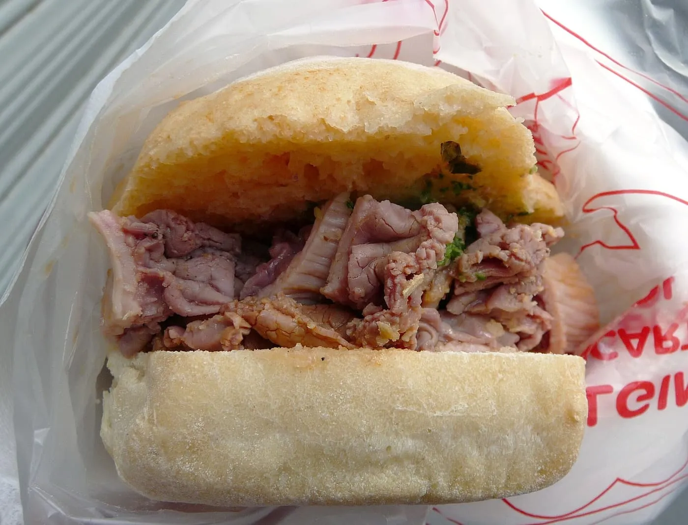 A lampredotto sandwich in a paper wrapper: a soft white roll filled with sliced tripe