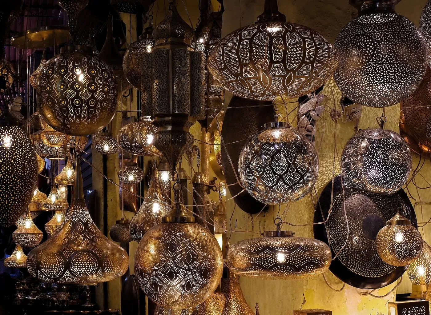 Pierced metal lamps and lanterns hanging together in a lit stall