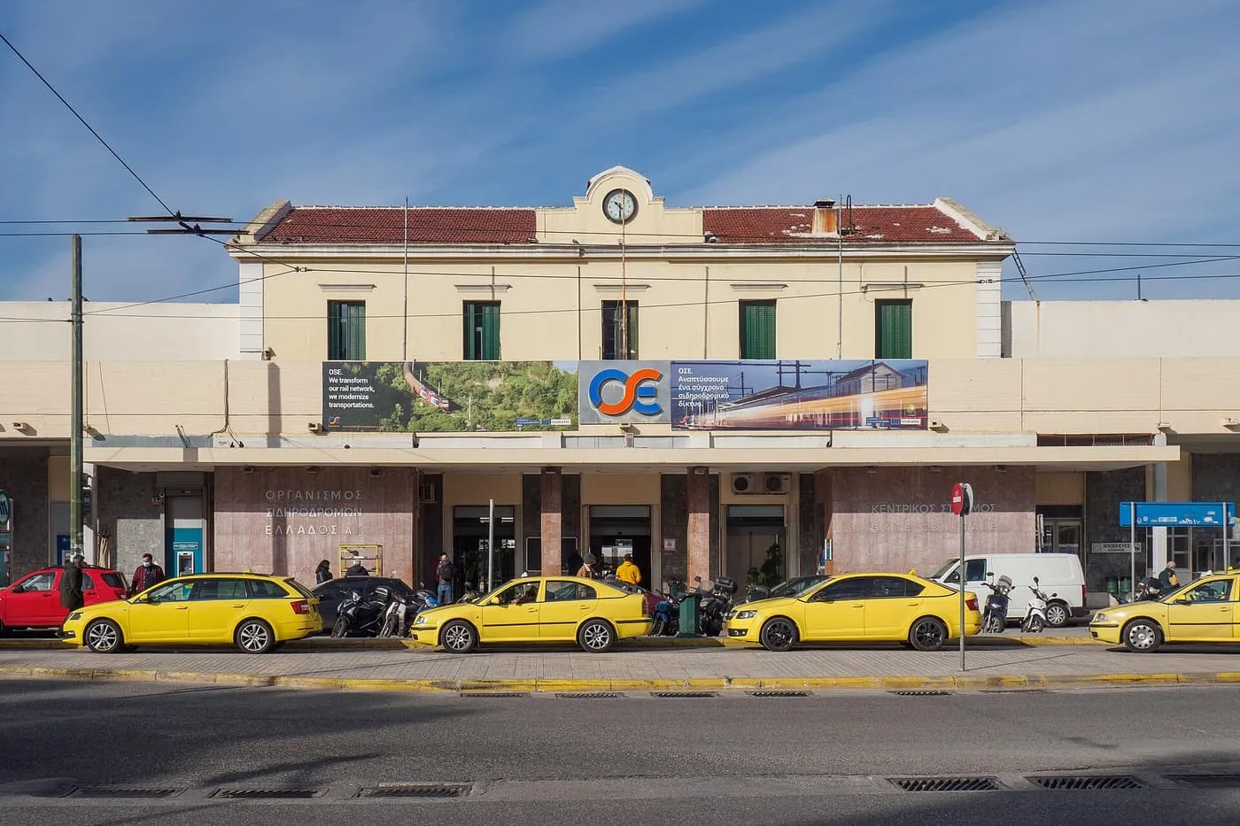 The cream-coloured front of Larissa railway station in Athens, with a row of yellow taxis at the kerb