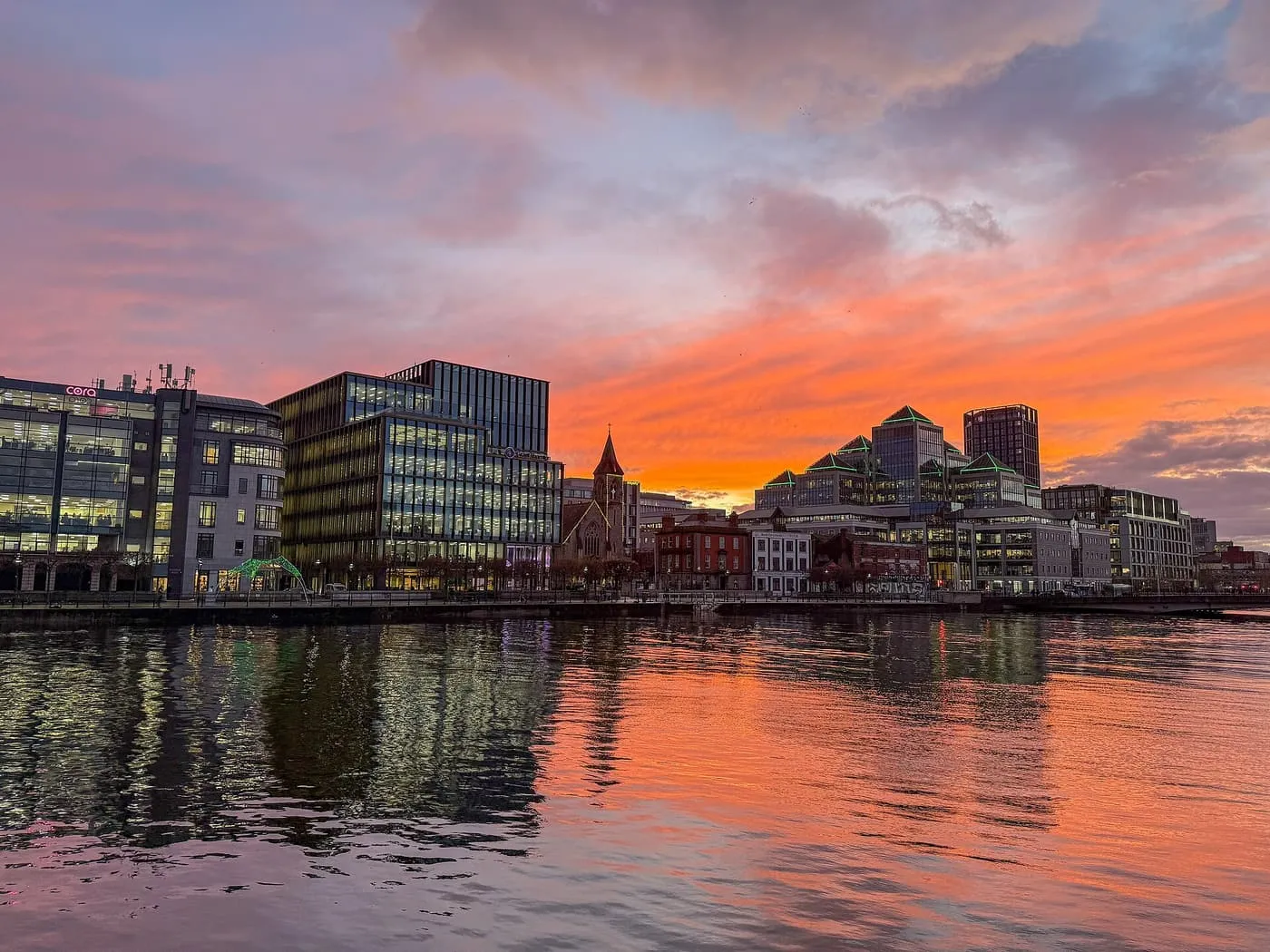 The Liffey at sunset, with glass office buildings on the far quay reflected in the water under a pink and orange sky