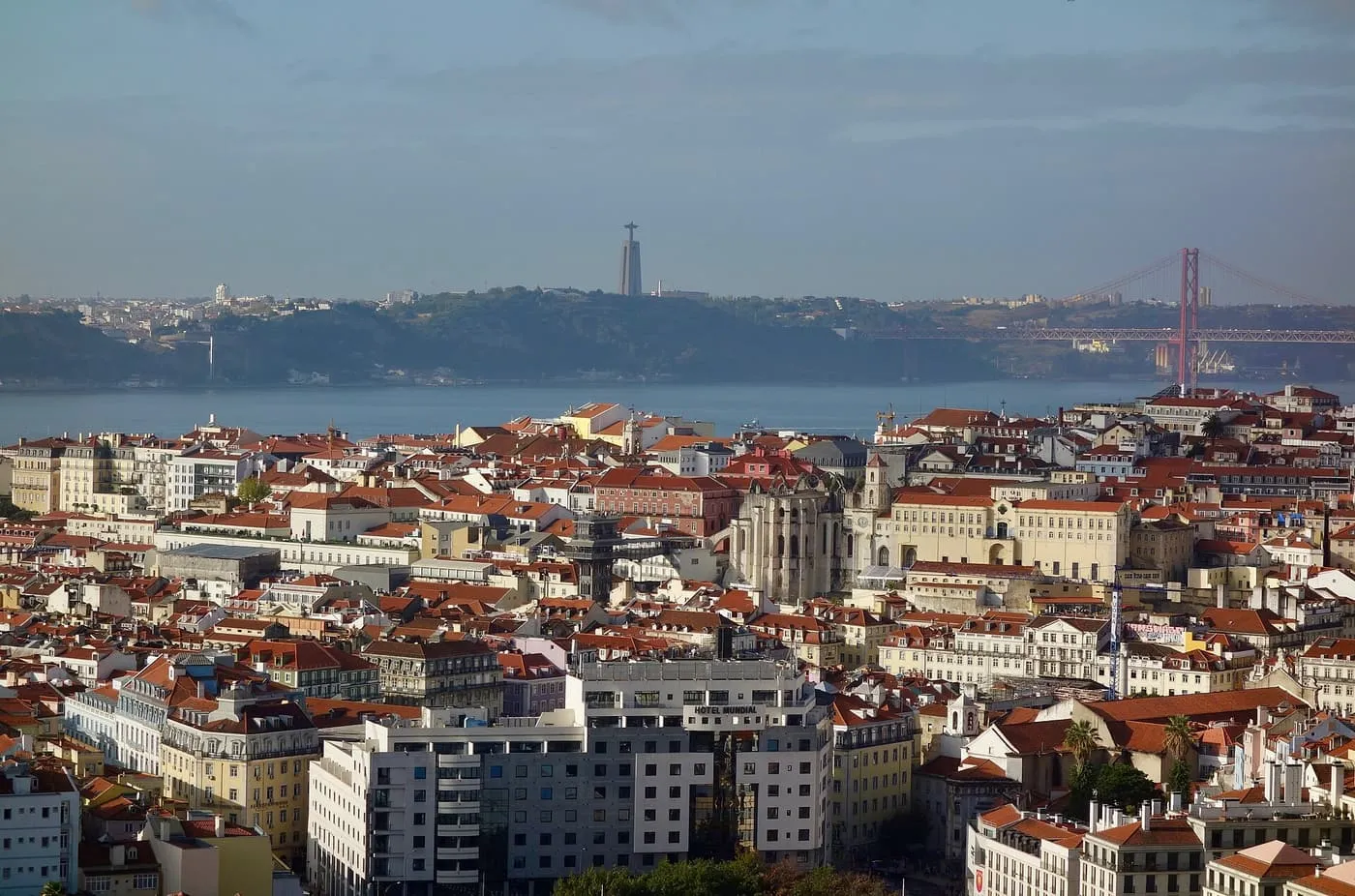 Red roofs of Baixa and Chiado from the hills, with the Carmo Convent ruins, the 25 de Abril Bridge and the Cristo Rei statue across the Tagus