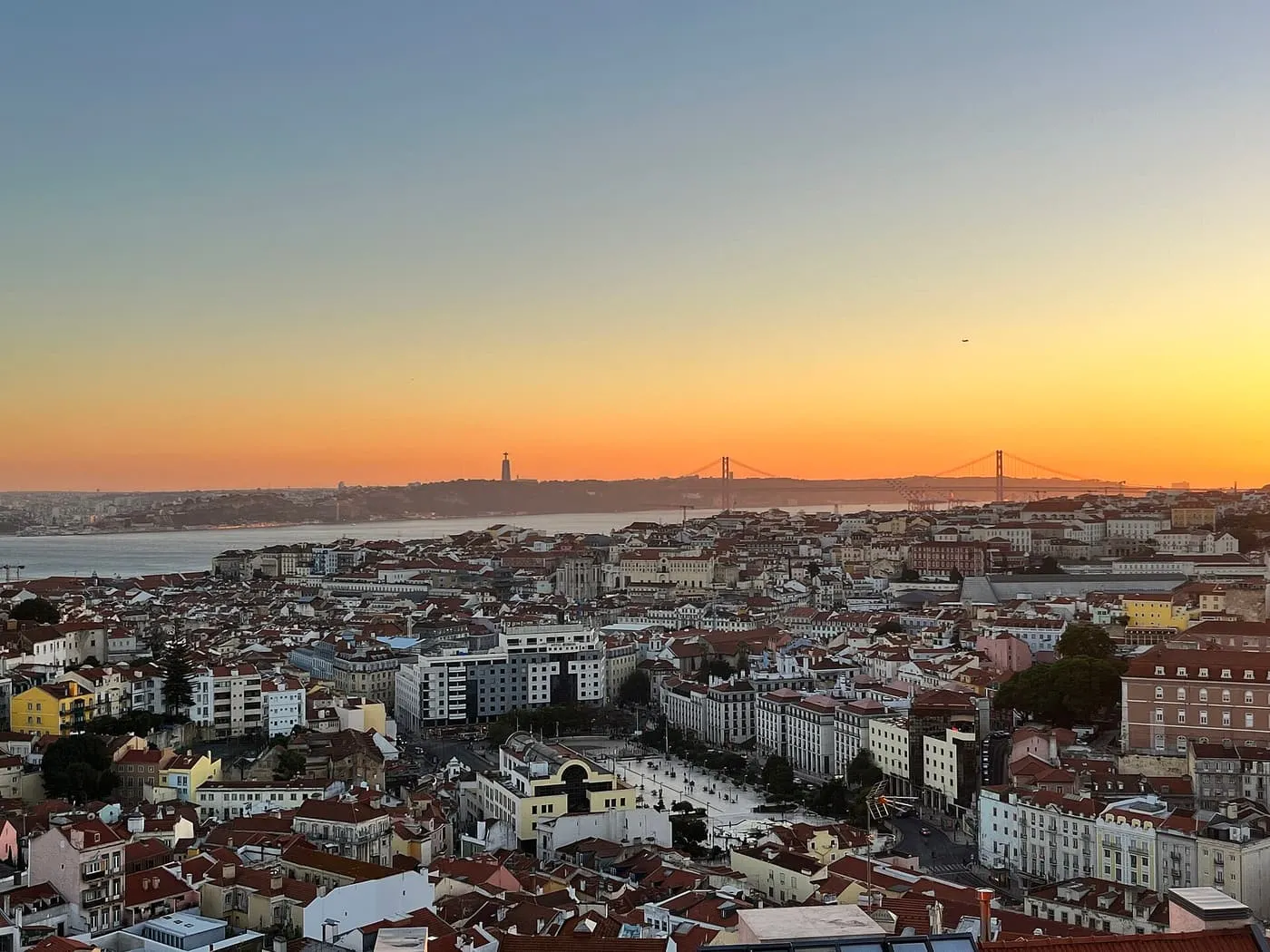 Orange sunset over the red roofs of Lisbon and the 25 de Abril Bridge, seen from the Miradouro da Graça