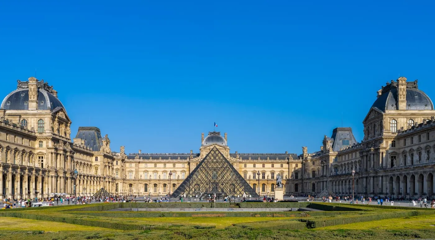 The Cour Napoléon of the Louvre, with the glass pyramid between the palace wings under a clear blue sky