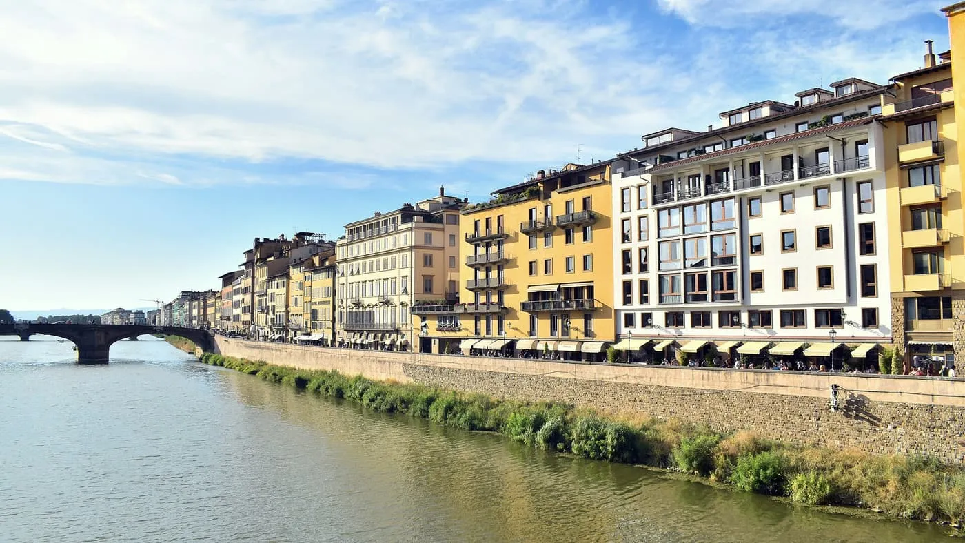 Cream and ochre buildings along the Lungarno degli Acciaiuoli beside the Arno, with a bridge in the distance