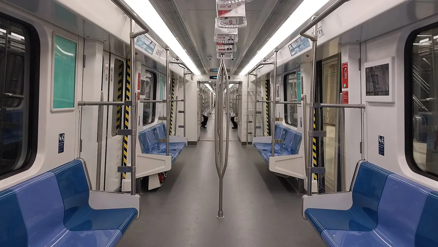 The inside of an empty M11 metro train, with blue seats along both sides and an open gangway through the carriages
