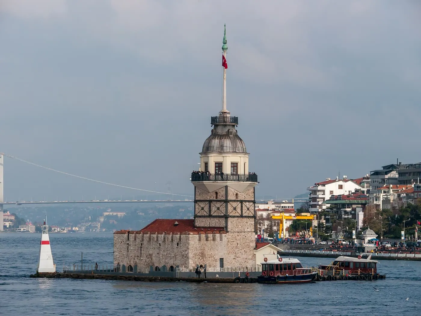 The Maiden's Tower on its rock in the Bosphorus, with a red and white beacon beside it and the Bosphorus Bridge in the haze behind