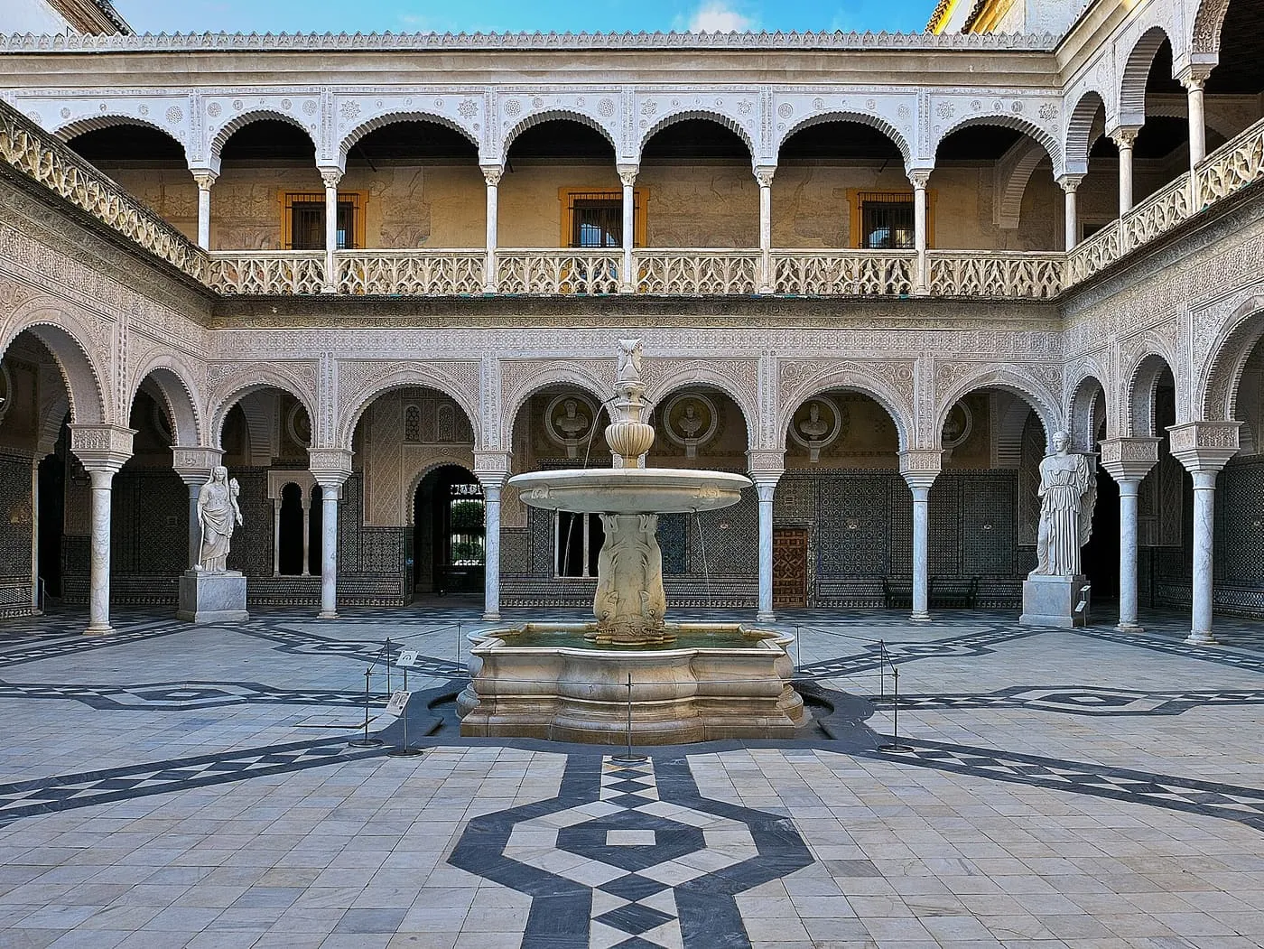 The main courtyard of the Casa de Pilatos, with a marble fountain, two statues and tiled walls under two floors of arcades