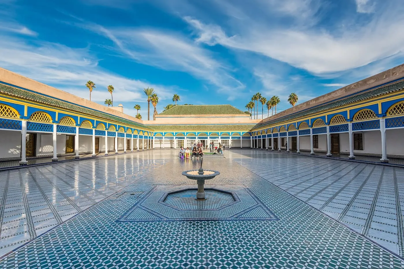 The large courtyard of the Bahia Palace, with a tiled floor, a central fountain and arched galleries painted blue and yellow
