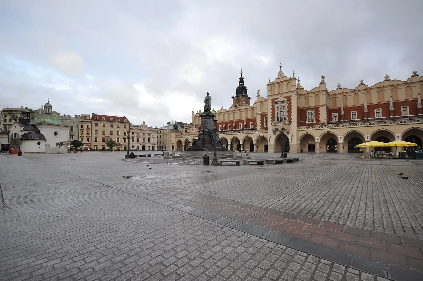 The Cloth Hall and the Adam Mickiewicz monument across the empty paved Main Market Square under a cloudy sky