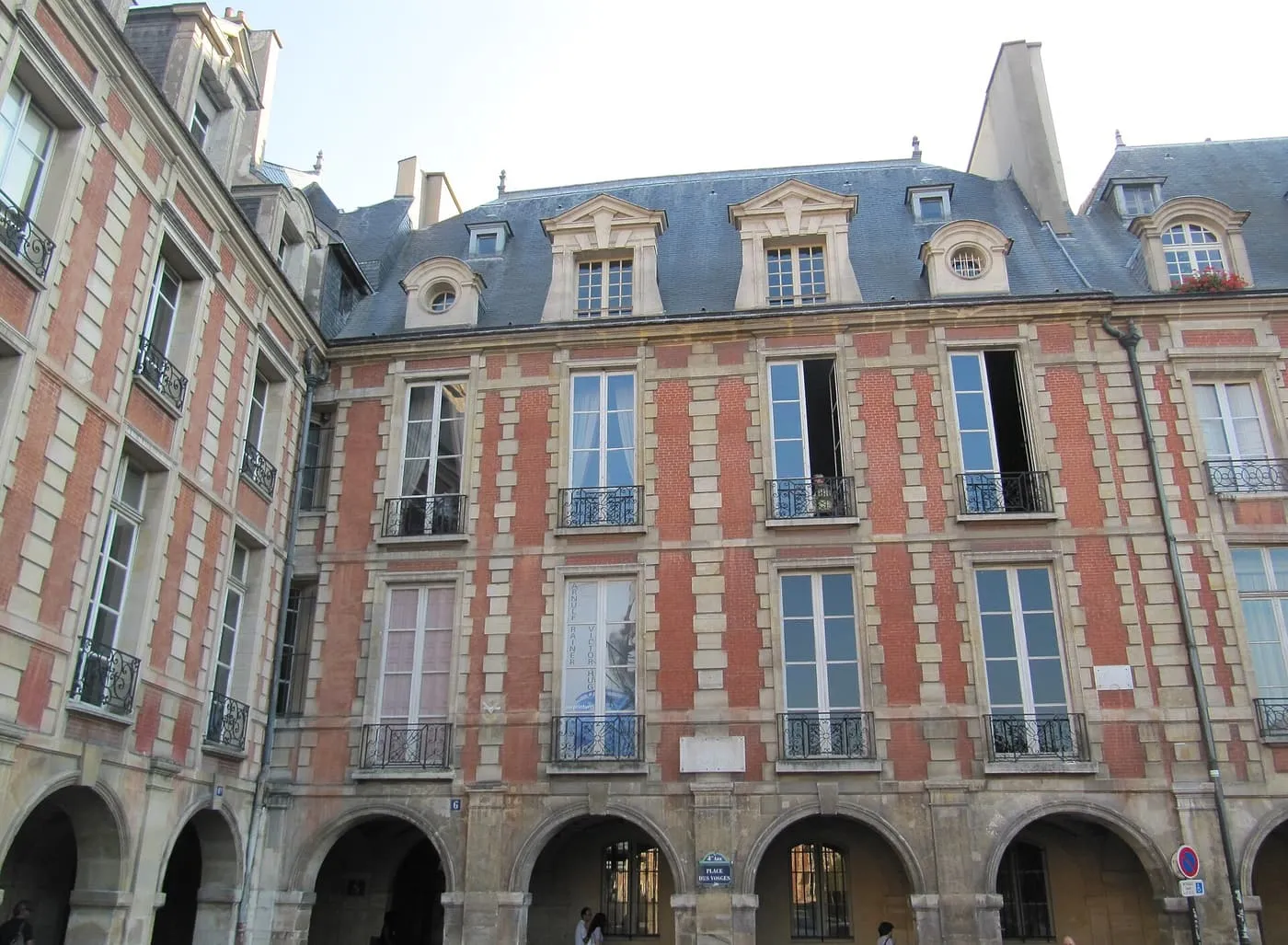 The brick and stone front of No. 6 Place des Vosges above the arcade, with tall windows and a slate roof