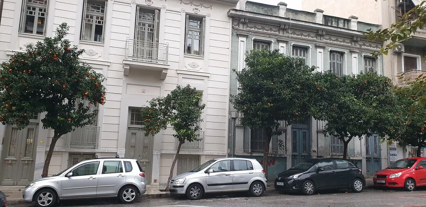 A street of neoclassical houses in Makrygianni with orange trees in fruit along the pavement and cars parked beneath them
