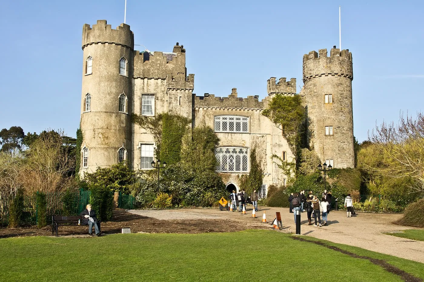 The grey stone front of Malahide Castle with two round towers and battlements, a gravel path and lawn in front
