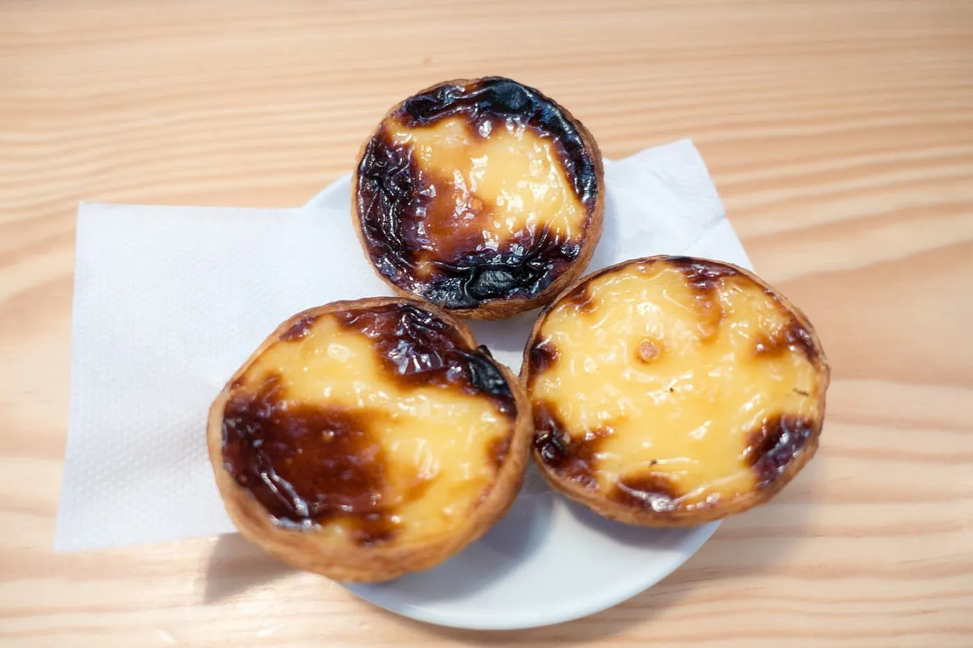 Three pastéis de nata on a small white plate, with blistered dark tops and set yellow custard