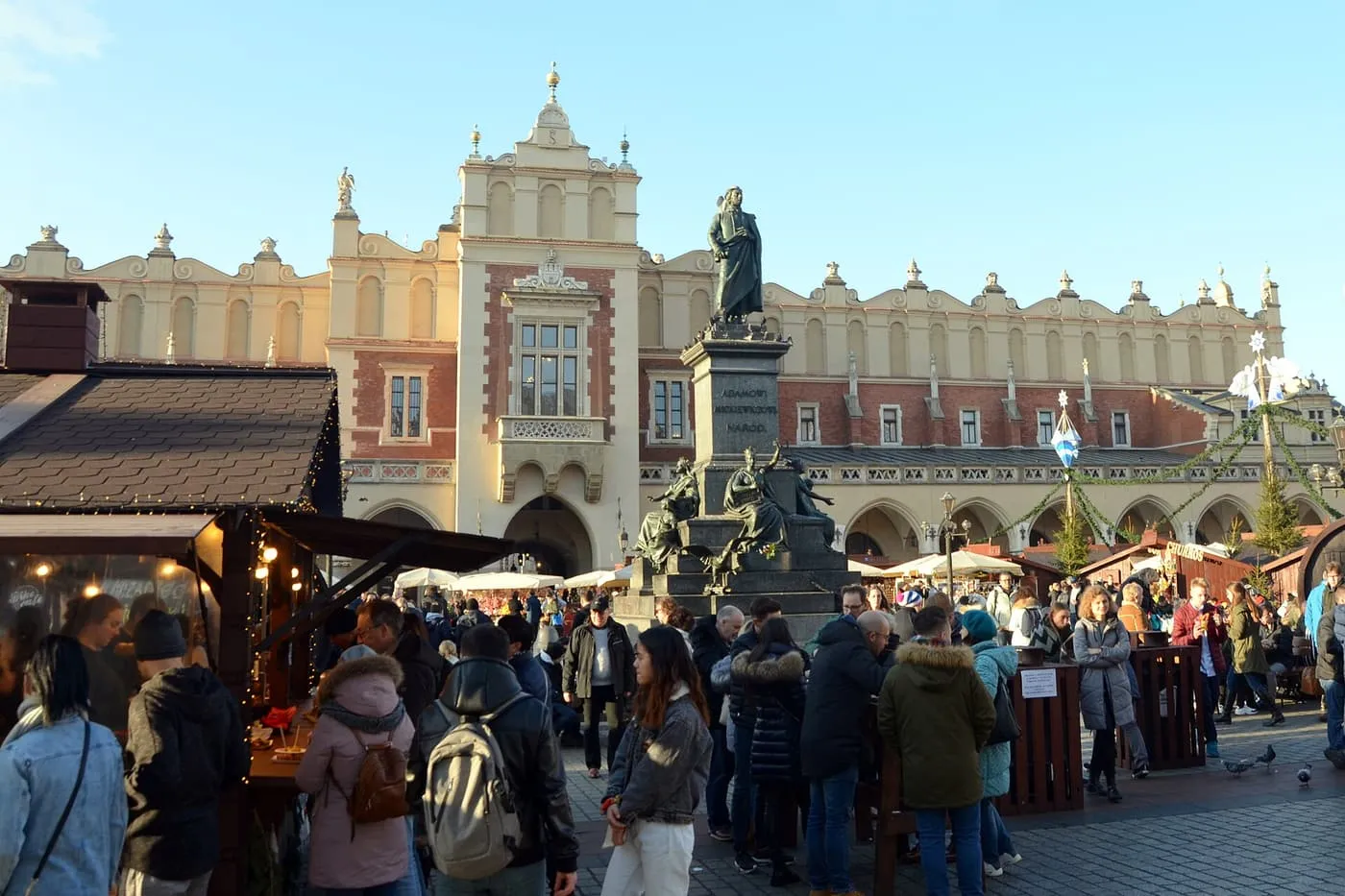 Wooden Christmas market stalls and crowds in front of the Adam Mickiewicz monument and the Cloth Hall on the Main Market Square