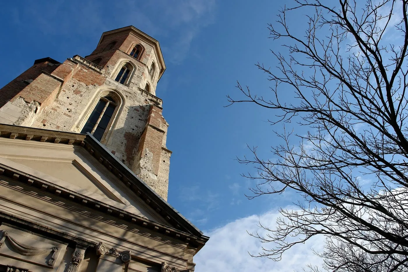 The brick Gothic Mary Magdalene Tower seen from below, against a blue sky and bare branches