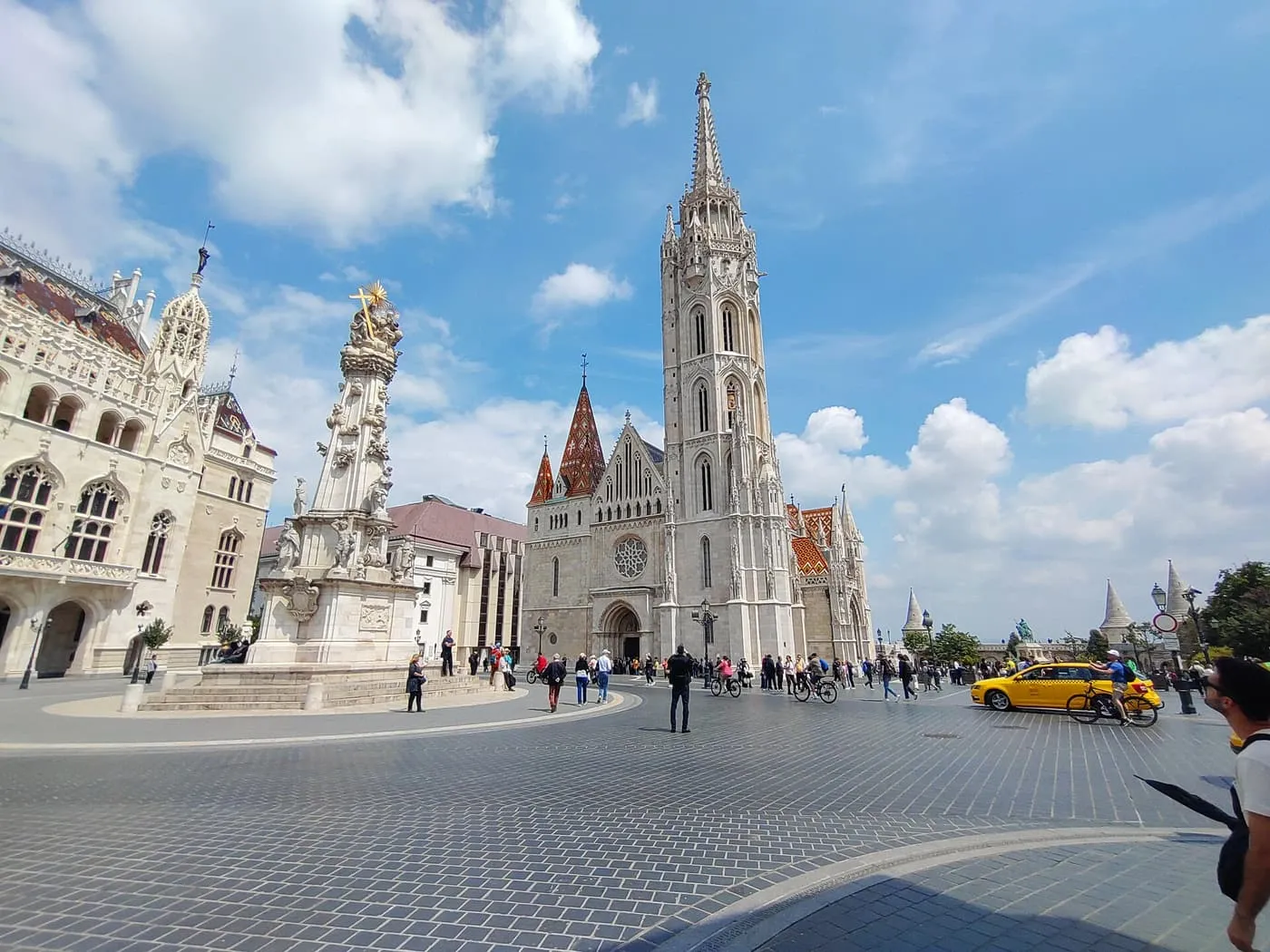 Matthias Church's tall grey spire and tiled roof beside the Holy Trinity Column on a paved square
