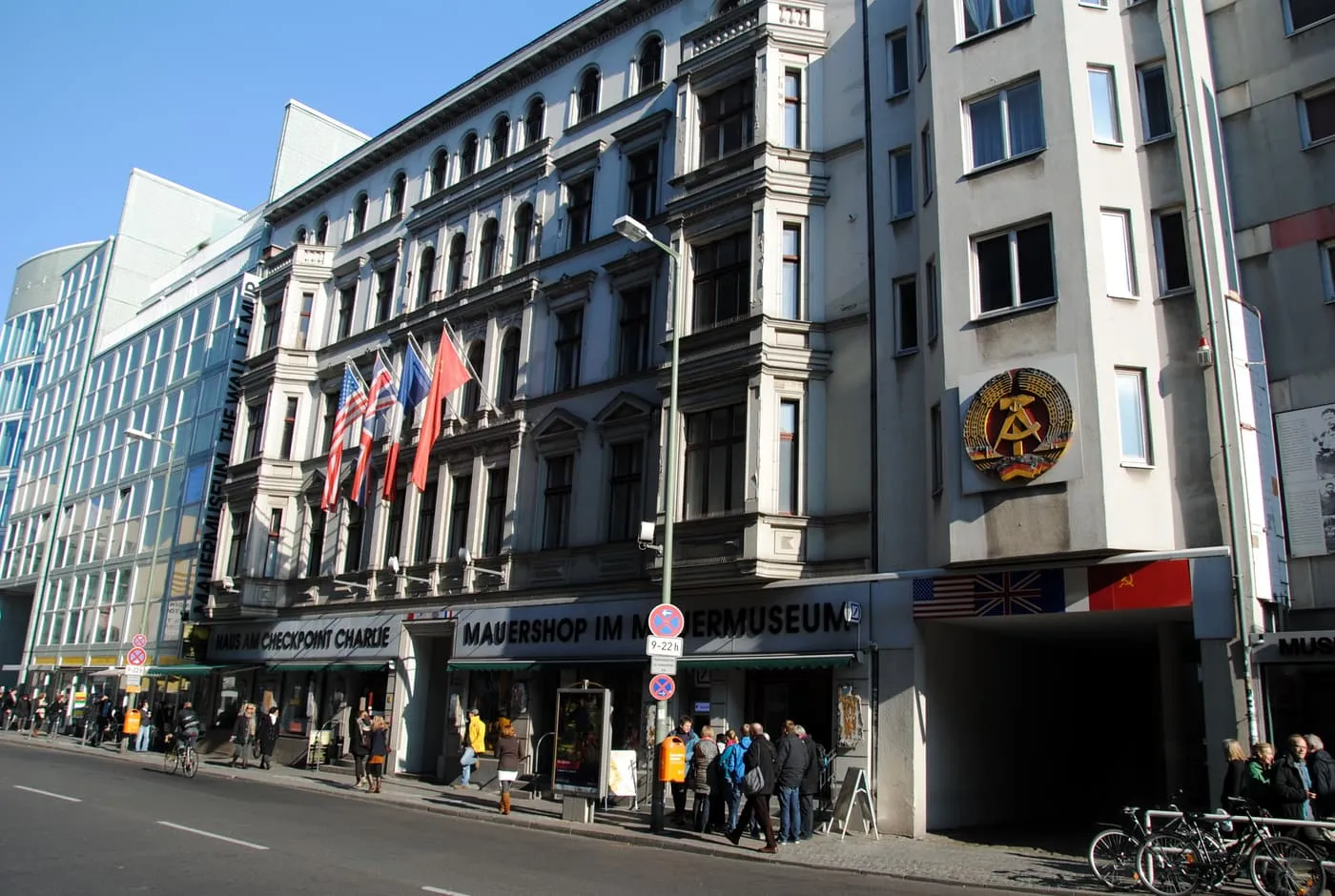 The street front of the Mauermuseum on Friedrichstraße, with national flags above the entrance and an East German emblem on the corner of the building