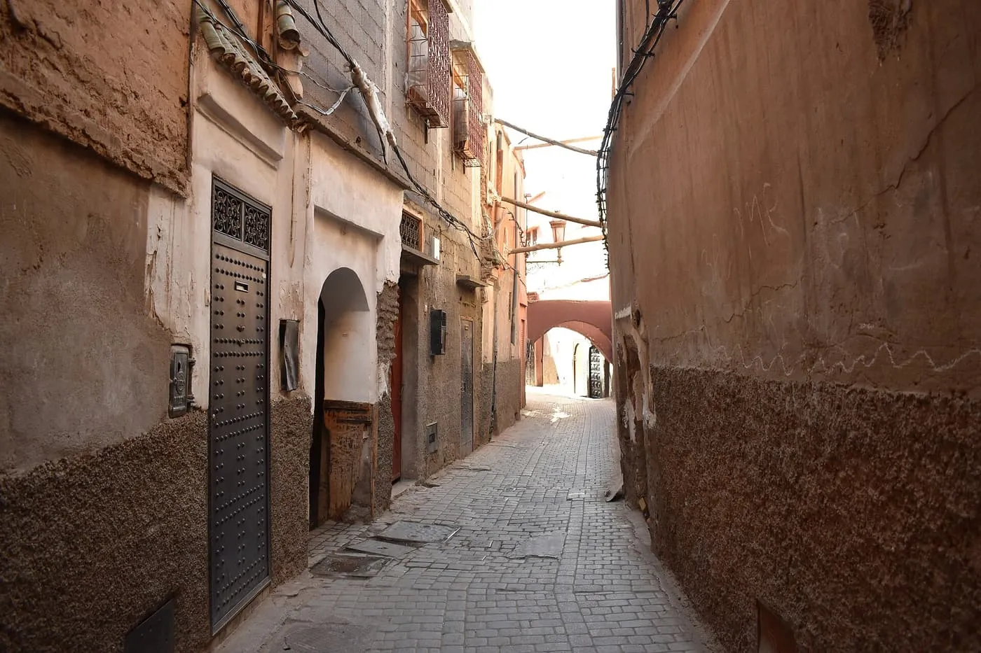 A narrow paved lane between high clay-coloured walls, with an arch in the distance