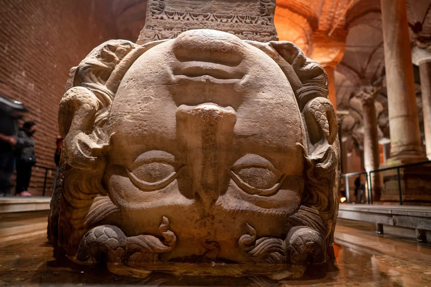 A carved Medusa head set upside down as the base of a column, standing in shallow water