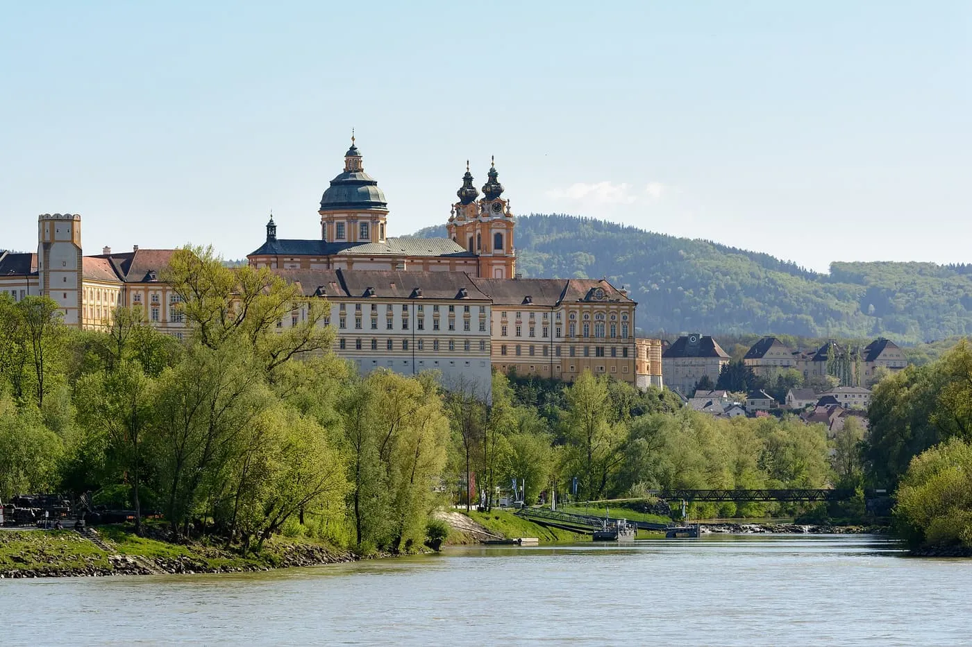 Melk Abbey's domed church and long yellow and white wings above the Danube, seen through trees on the bank
